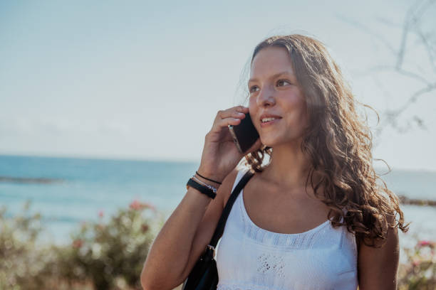 istock A woman is talking on her cell phone while standing on a beach on a summer day 2178535972