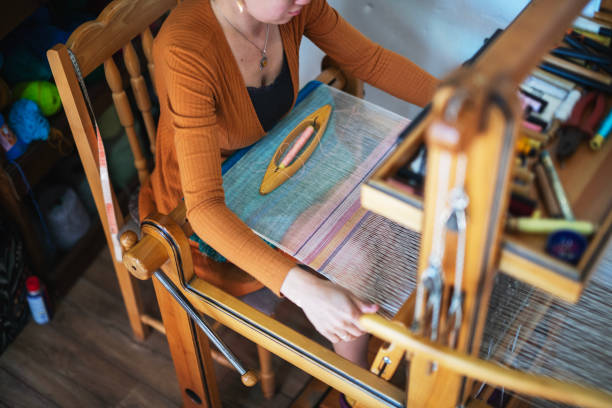 Shot of young woman having an incredible skill in weaving.She is sitting on a loom and weaving a beautiful rug.