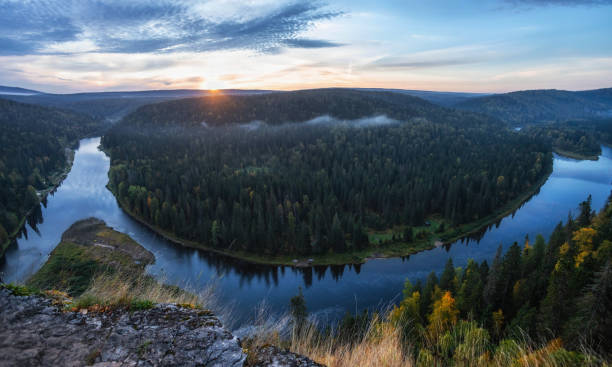 istock A breathtaking landscape shows a winding river cutting through dense forests, with the warm glow of sunset illuminating the scene and casting reflections on the water 2178539037