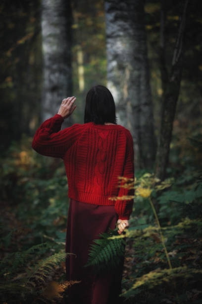 istock Woman clad in a cozy red sweater waves while exploring a tranquil forest, surrounded by dense trees and vibrant ferns in soft evening light 2178539057