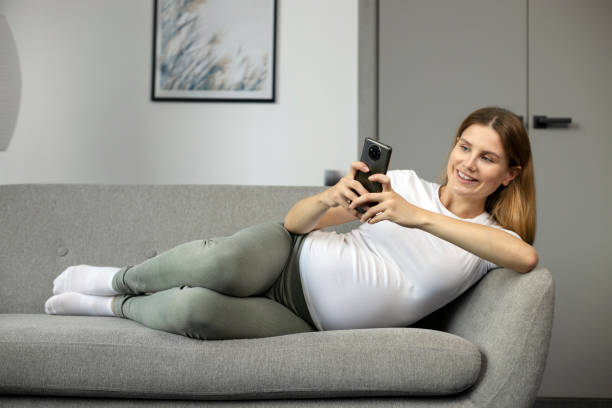 istock Pregnant woman relaxing on sofa using smartphone 2178539568