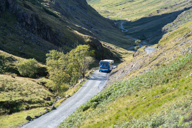 A solitary bus navigates the winding roads of the Lake District, surrounded by dramatic hills and serene landscapes.