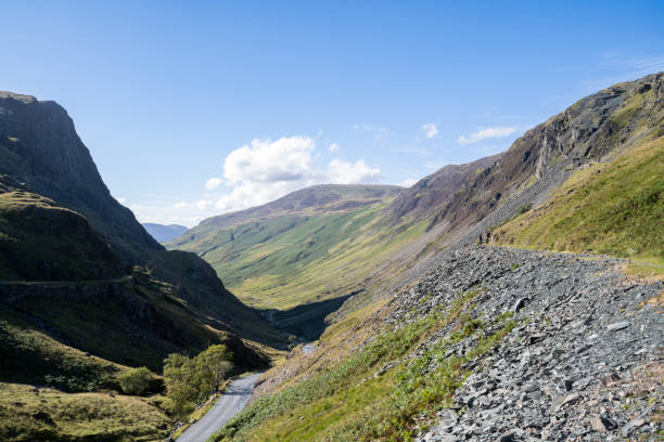 A winding road cuts through the lush green hills of the Lake District, offering a peaceful escape into nature's beauty.