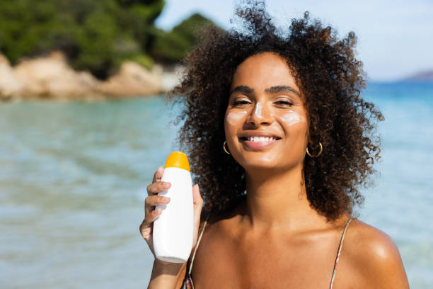 istock Cheerful young lady applying sunscreen while having fun at the beach 2178546339