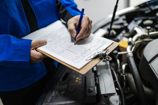A mechanic inspects a vehicle, documenting findings on a clipboard during a maintenance check at an auto repair shop