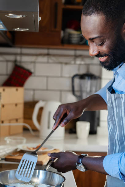 istock A young, smiling African-American man cooking eggs for breakfast in his modern kitchen. He is enjoying a peaceful morning while preparing his meal in a bright and stylish space. 2178552902