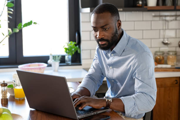 istock A focused African-American man works on his laptop at a kitchen counter. The modern kitchen is well-lit, with fresh fruit and a glass of juice nearby, creating a productive atmosphere. 2178552971