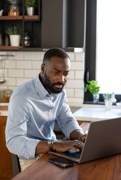 istock A focused African-American man works on his laptop at a kitchen counter. The modern kitchen is well-lit, with fresh fruit and a glass of juice nearby, creating a productive atmosphere. 2178552975