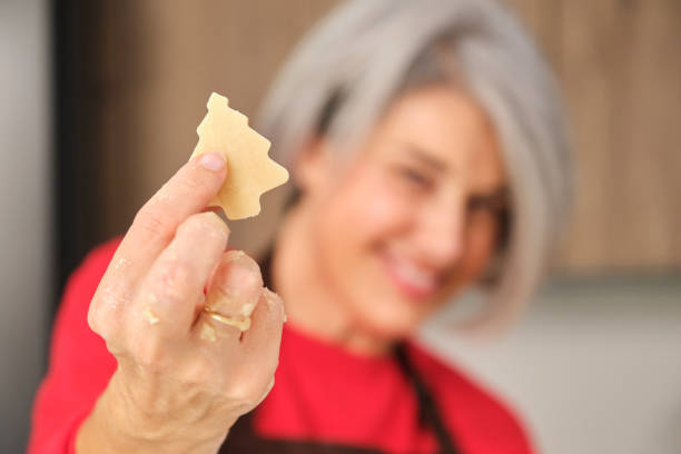 Woman is holding a Christmas tree shaped cookie in her hand and smiling