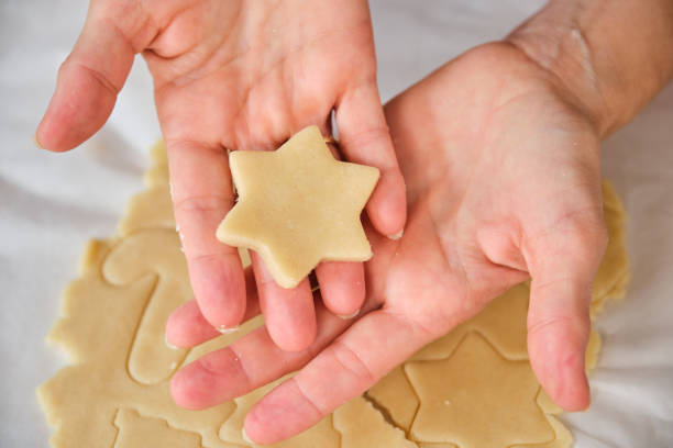 Woman showing a star shaped cookie dough from a baking sheet full of Christmas cookies with different shapes, ready to bake
