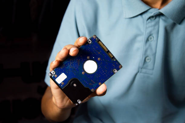 A male technician holds a 2.5-inch hard drive, a data storage device.