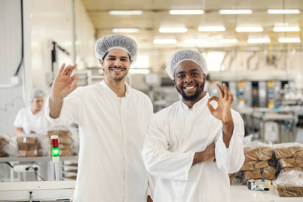 istock Two interracial food factory workers in sterile uniforms gesturing okay and smiling at camera. 2178564115