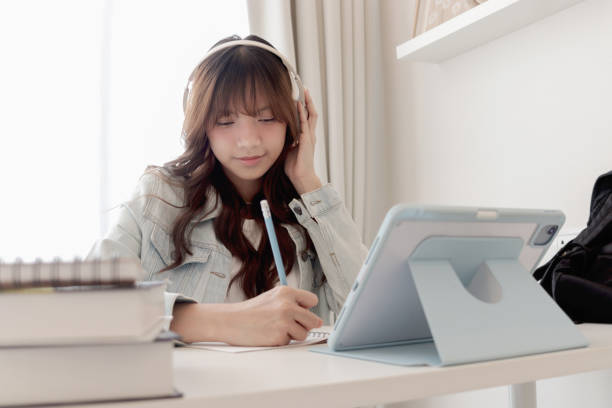 istock Happy Asian woman wearing headphones takes a note during using digital tablet to study online tutorials on video platforms. Beautiful smiling female teenager girl studying online and doing homework by using tablet device. Technology and educational concep 2178565170