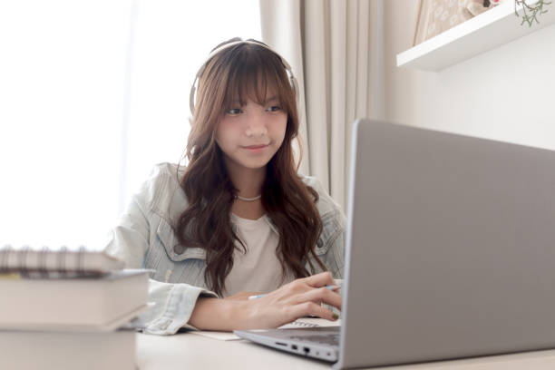 istock Happy Asian woman wearing headphones using laptop to study online tutorials on video platforms. Beautiful smiling female teenager girl studying online and doing homework by using computer. Technology and educational concept. 2178565188