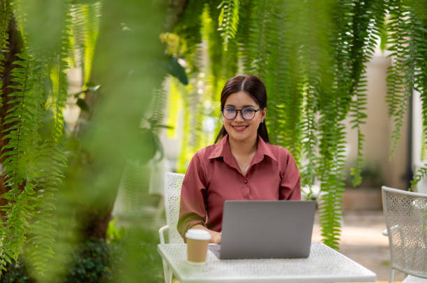 istock Young professional woman using a laptop while sitting in a comfortable wicker chair surrounded by lush greenery. 2178579232