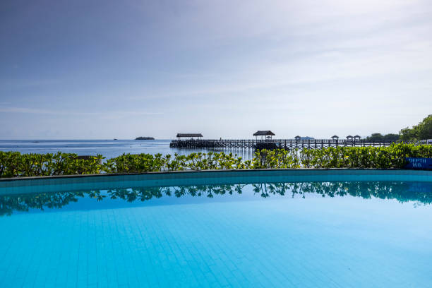 A luxurious infinity pool offers breathtaking views of the tranquil waters of Thailand. The sun begins to set behind the horizon, casting golden hues across the sky and water.