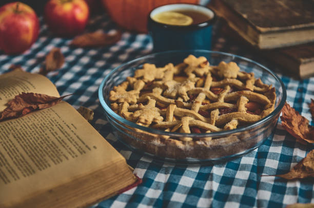 istock Homemade apple pie on a rustic table with a checkered cloth, surrounded by books, apples, and dried leaves, evoking a cozy and autumnal atmosphere perfect for storytelling and tea time. 2178580861