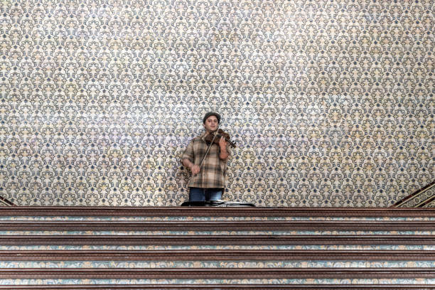 SevillaÂ  Sevilla - Spain - 04-19-2024: A street musician plays violin in front of decorative tilework at Plaza de EspanaÂ  adding charm to the ambiance.