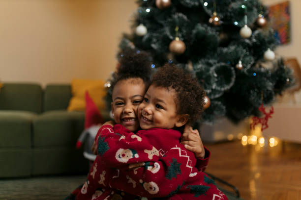 istock Cute siblings in matching sweaters hugging by christmas tree 2178604080