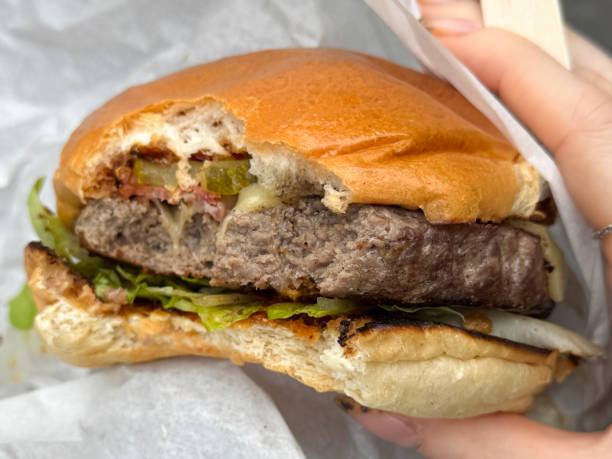 Stock photo captures the perfect moment of taking a bite into a delicious cheeseburger. The soft burger bun cradles a juicy patty, fresh lettuce, and vibrant salad, all complemented by a generous drizzle of ketchup