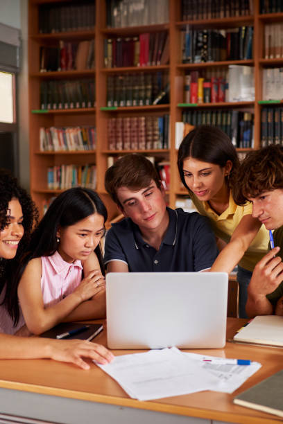 istock Group of students at library gathering together to do a school project as teamwork using a laptop. 2178607146