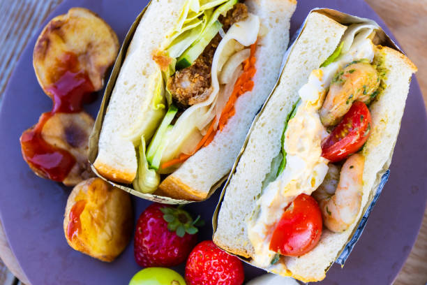 A close up directly above view of colorful professionally made sandwiches with various organic ingredients along with potato wedges and fruit.