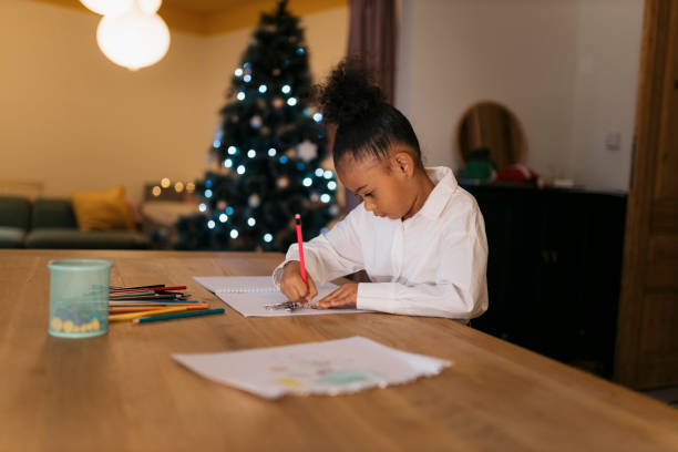 istock Little girl drawing at table with christmas tree in background 2178613713