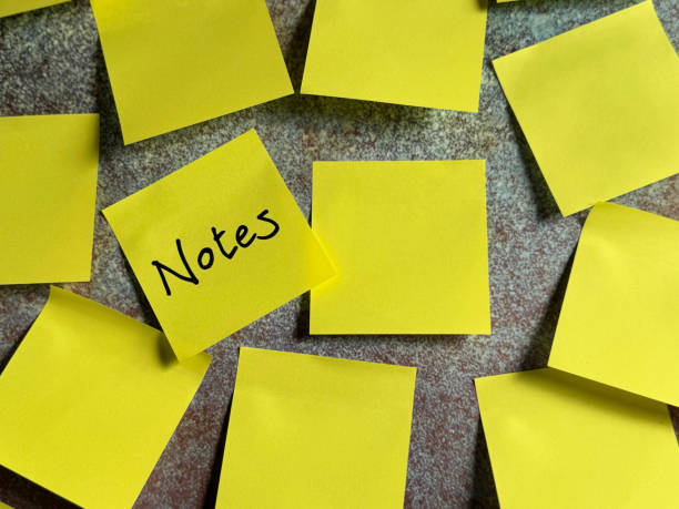 Stock photo showing close-up view of wall papered with a group of yellow adhesive notes available for messages with one yellow paper square having the word 'Notes' written in black marker pen. Ideation, creative thinking and idea storming concept.