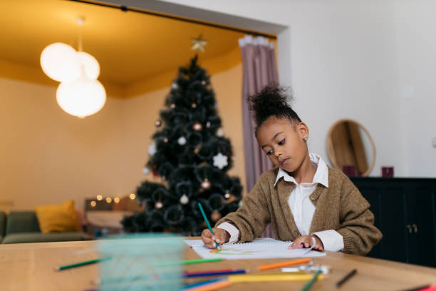 istock Small girl drawing at table with Christmas tree in background 2178614014