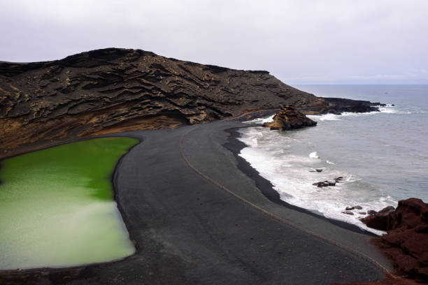 aerial view of Charco Verde against foamy ocean on a beach of black sand in Yaiza, Lanzarote at Canary Islands, Spain, Concept of wild nature and volcanic landscape