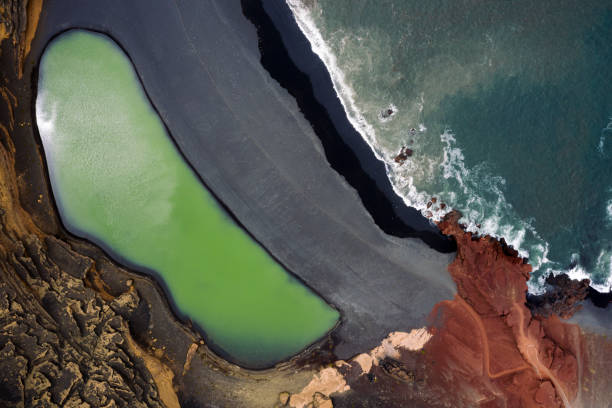 top view of Charco Verde against foamy ocean on a beach of black sand in Yaiza, Lanzarote at Canary Islands, Spain, Concept of wild nature and volcanic landscape