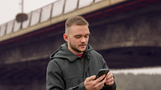 istock A Young Man Texting on His Phone While Standing Near a Bridge on a Cloudy Day 2178626662