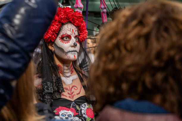 A participant in Barcelona's Day of the Dead parade wears a vibrant red flower crown and intricate face paint, celebrating the cultural fusion of Halloween and Day of Dead.