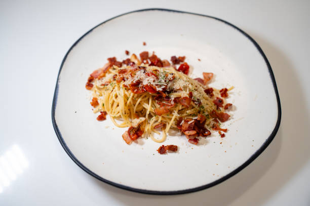 On a checkered tablecloth, a plate brimming with spaghetti rests beneath the dappled shadows of vine leaves cast against a lime-washed wall, evoking a sun-kissed Mediterranean breeze
