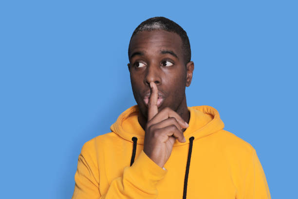 istock Man in yellow hoodie gesturing for silence 2178660104