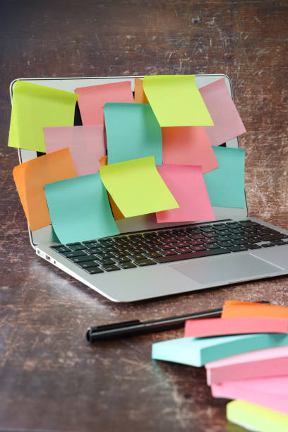 istock Image of open laptop with screen covered in multicoloured sticky notes, overlapping blank adhesive papers for note taking, yellow, orange, turquoise blue and pink paper squares, black ball point pen, fallen stack of sticky note pads 2178660267