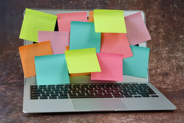 istock Close-up image of open laptop with screen covered in multicoloured sticky notes, overlapping blank adhesive papers for note taking, yellow, orange, turquoise blue and pink paper squares, stationery, brown background, focus on foreground 2178660388