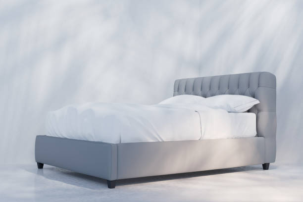 istock Side view of bed with white linen. Light and shadows on white wall 2178660447