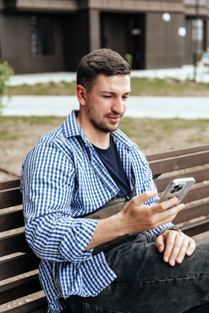 istock Young man sitting on a bench in a park 2178666791
