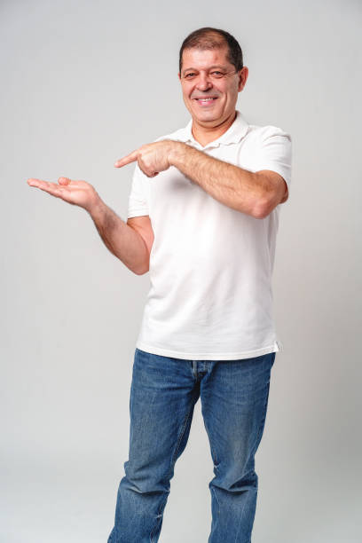 istock Man dressed in a white polo shirt and jeans happily pointing to the side against a plain background 2178667232