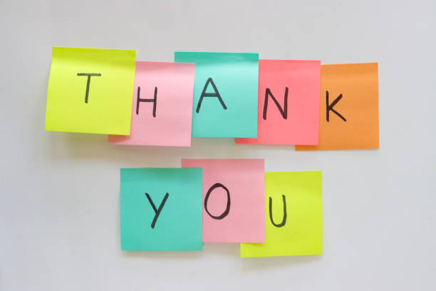 Stock photo showing close-up view of wall with eight multicoloured adhesive notes stuck in two rows of five and three, with individual, capital letters written in black marker pen spelling out 'Thank You'. Ideation, creative thinking and idea storming concept.
