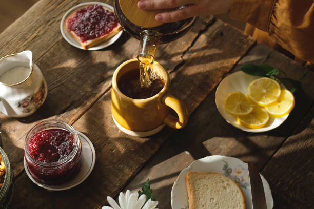 Female hands pouring tea from teapot during morning breakfast in kitchen.