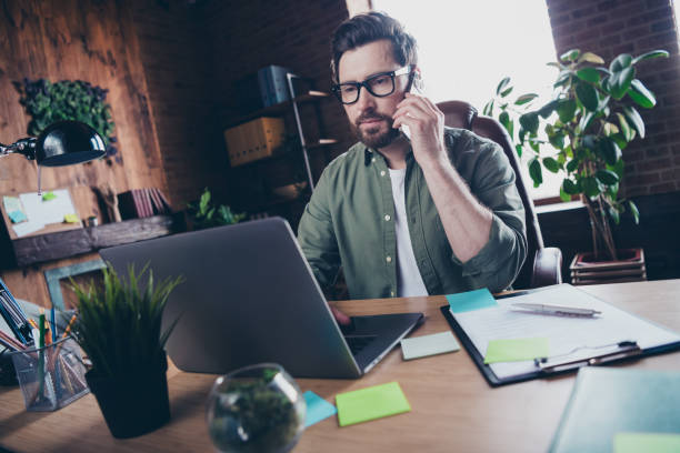 istock Photo of handsome young guy work netbook talking phone dressed green shirt comfortable startup office loft room interior 2178673477