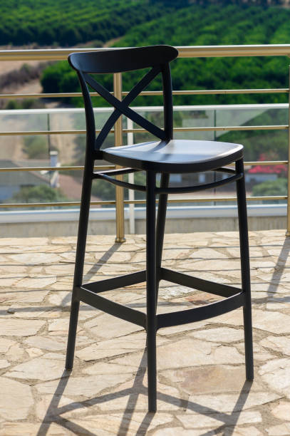 Elegant Black Bar Stool on a Sunny Terrace Overlooking Lush Greenery and Fields in a Serene Outdoor Setting
