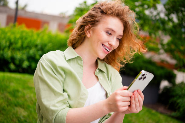 istock Young redhaired woman enjoying sunny day outdoors, relaxing and smiling while using smartphone in a lush green park setting 2178678199