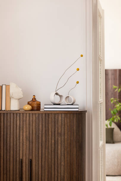 istock Stylish interior with a wooden cabinet adorned with potted plants, decorative objects, and books. A vibrant art piece featuring a sunburst design adds a pop of color. Cozy seating area visible in the background. 2178680359