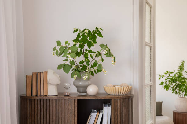 istock Stylish interior with a wooden cabinet adorned with potted plants, decorative objects, and books. A vibrant art piece featuring a sunburst design adds a pop of color. Cozy seating area visible in the background. 2178680404