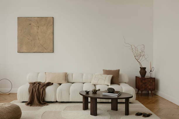 A serene, minimalist living room with a plush, white sofa adorned with neutral cushions and a cozy blanket. A wooden coffee table, abstract wall art, and elegant decor complete the tranquil ambiance.