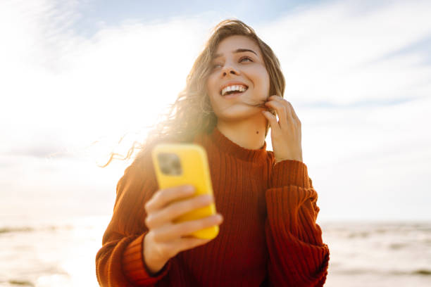istock Young woman using mobile phone at beach. Cold weather. Autumn. 2178686184