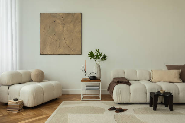 istock A modern living room interior featuring cozy, plush white sofas, a wooden side table with decorative items, and minimalist decor. The space is enhanced by a large abstract painting and a soft rug, creating a warm, inviting atmosphere. 2178686548